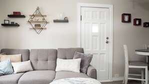 A living room with a grey sofa, a white door, and a dining area with a white table and chair. - Cozy Bancroft Stay in the Minnow Lake area (Greater Sudbury)