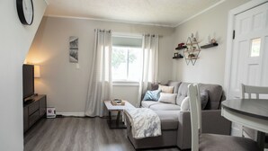 A cozy living room with a sofa, a TV, and a dining table. - Cozy Bancroft Stay in the Minnow Lake area (Greater Sudbury)