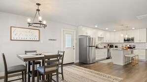 Une cuisine moderne avec des meubles blancs, un réfrigérateur en acier inoxydable et un coin repas comprenant une table et des chaises en bois.