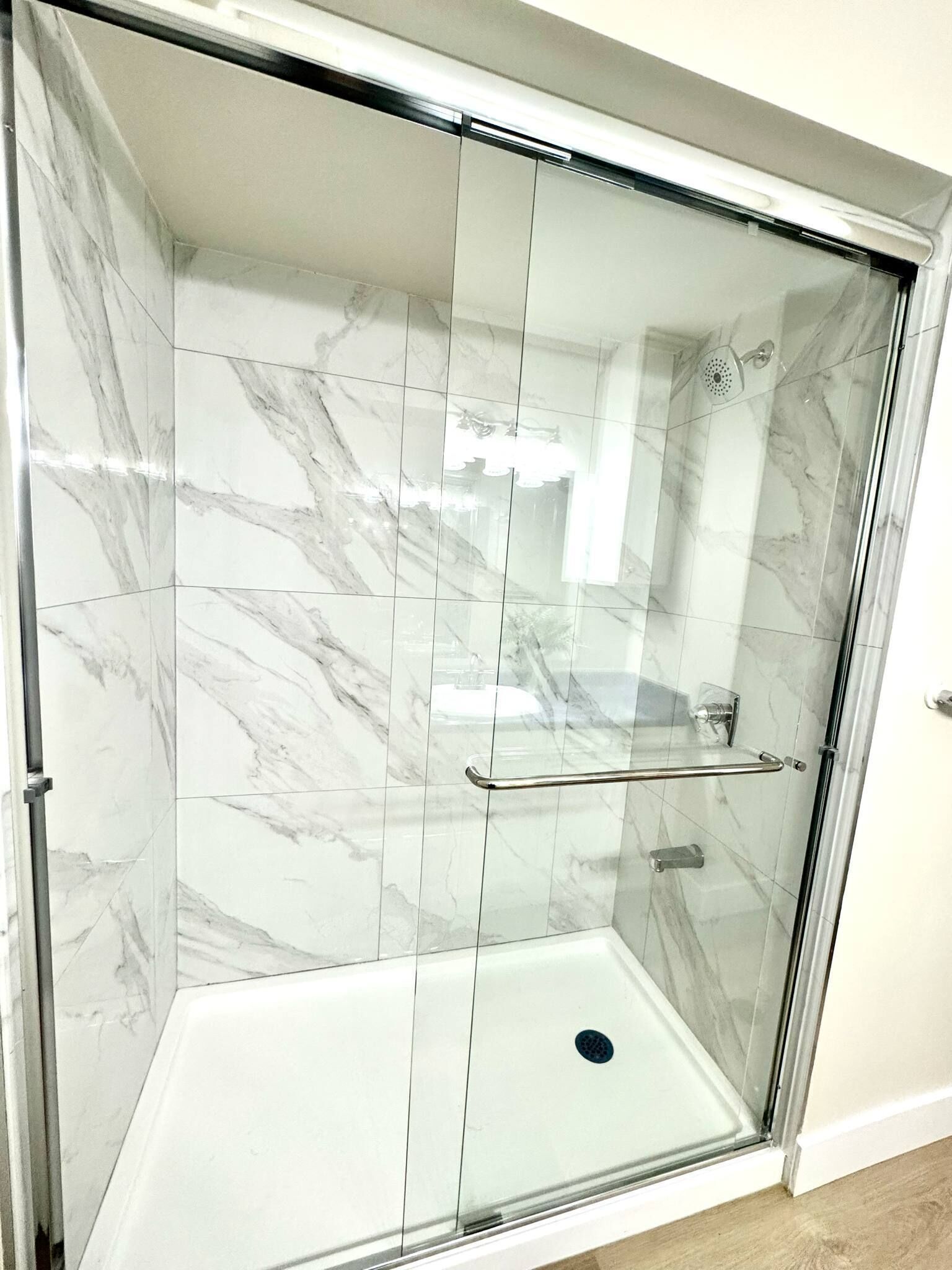A glass-enclosed shower with a marble tile interior and a metal handrail.