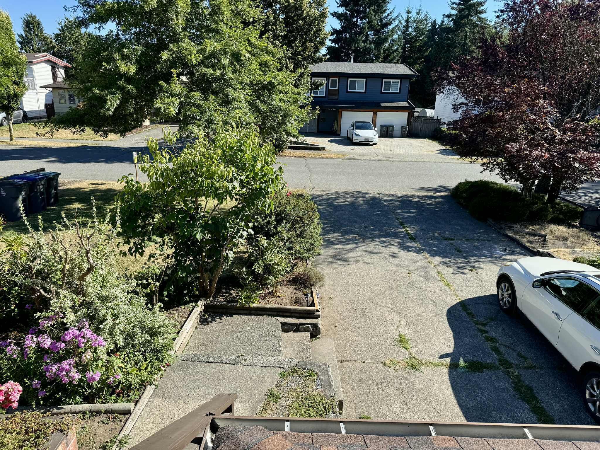 A residential driveway with a white car parked on the right, a garage door, and a house in the background.
