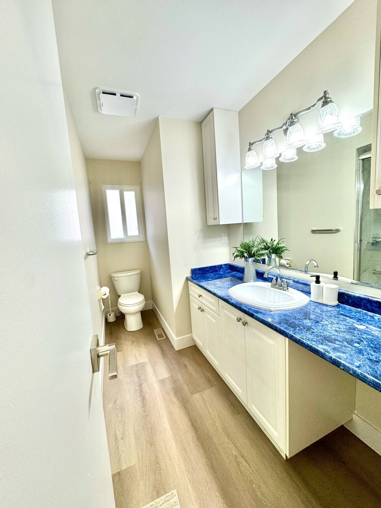 A modern bathroom with a white toilet, a sink with a blue marble countertop, and a mirror with lights above it.