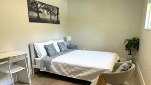 Een slaapkamer met een bed, een bureau, een stoel, een nachtkastje en een wandplant.
