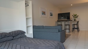 A bedroom with a bed, grey sofa, and a small kitchenette area with a TV and chairs. - Charming 2 Apartments in delightful Islington with AC, Balcony & Wifi. (Islington)
