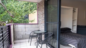 A balcony with a table and chairs, a sliding glass door to a bedroom with a bed and a wardrobe, and a tree outside. - Charming 2 Apartments in delightful Islington with AC, Balcony & Wifi. (Islington)