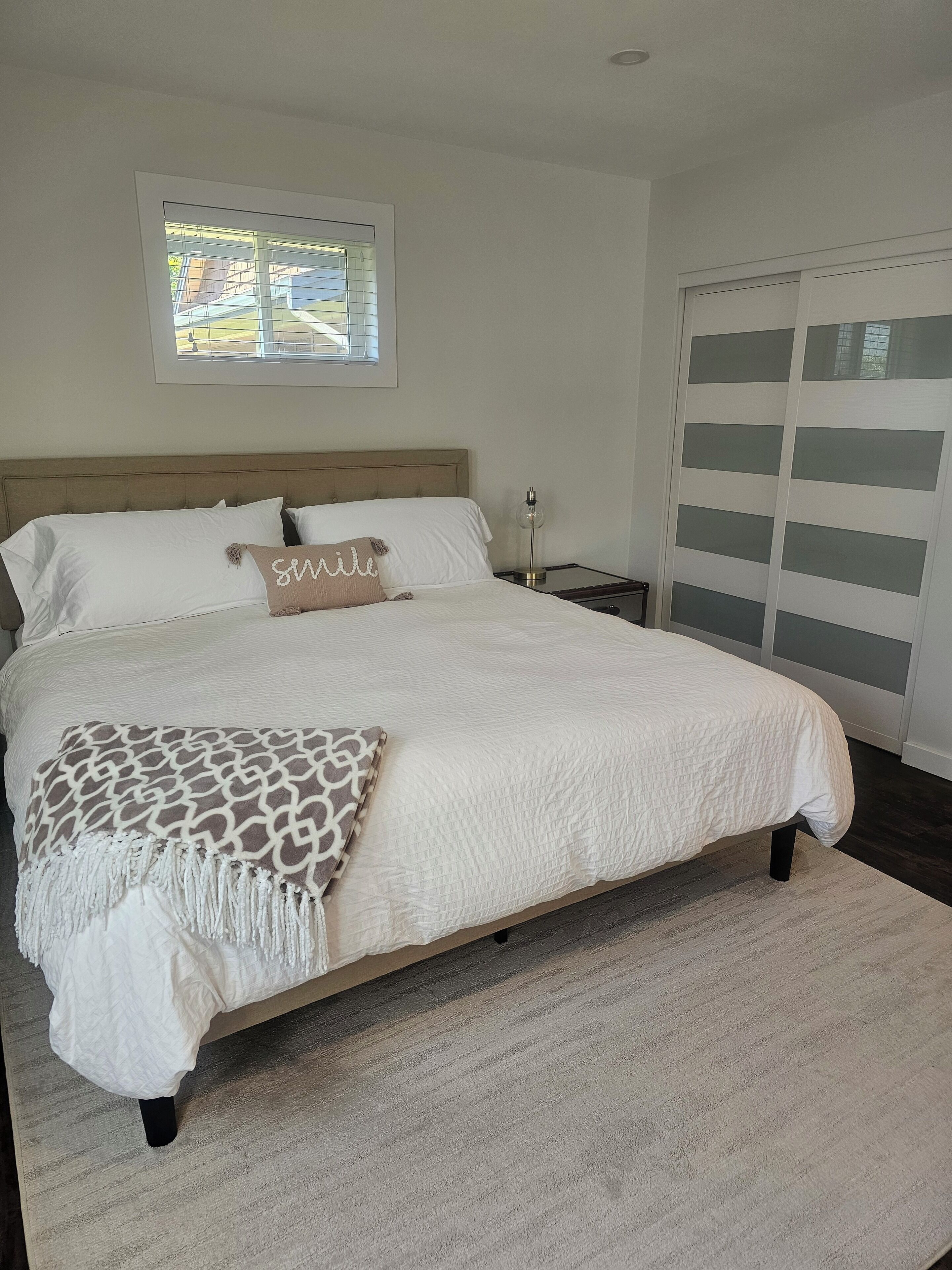 A bedroom with a large bed, a nightstand, a lamp, a window with blinds, and a sliding door.