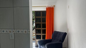 Una habitación con un sofá azul oscuro, una ventana con cortinas naranjas y un suelo de baldosas.