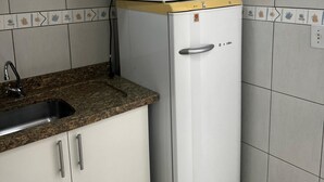 Una cocina compacta con armarios blancos, encimera de granito, microondas integrado y un refrigerador.