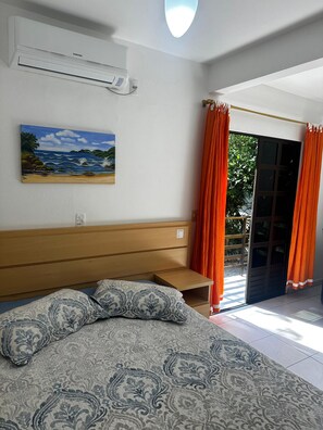Ein Schlafzimmer mit einem Bett, einem Gemälde, einer Klimaanlage und Blick ins Freie.