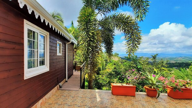 A wooden house with a tiled patio, surrounded by lush greenery and a scenic view. - 🌿 Kachiman Country Bungalow 🌿 (Saint-Esprit)