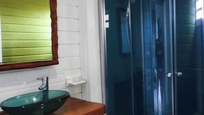 A bathroom with a wooden vanity, a green glass bowl sink, a white tiled wall, and a glass shower enclosure. - 🌿 Kachiman Country Bungalow 🌿 (Saint-Esprit)