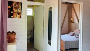 A room with a sloped ceiling, a bed with a patterned bedspread, a small table with a lamp, and a bathroom visible through an open door. - 🌿 Kachiman Country Bungalow 🌿 (Saint-Esprit)