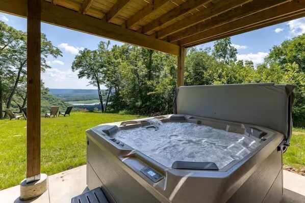 Un jacuzzi bajo una pérgola de madera, con un césped y árboles al fondo.