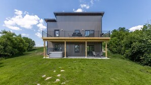 Une maison moderne à deux étages, dotée d’un balcon, d’un jacuzzi et d’une terrasse couverte.