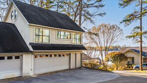 A two-story house with a garage, a driveway, and a view of a body of water. - One-bedroom treehouse loft with lake views, shared dock access, and full kitchen on Lake Hamilton. (Garland County)