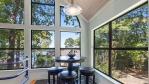 A room with large windows, a round table with stools, and a view of trees and a building outside. - One-bedroom treehouse loft with lake views, shared dock access, and full kitchen on Lake Hamilton. (Garland County)