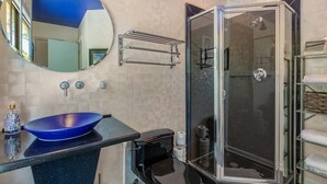 A bathroom with a round mirror, a blue sink, a glass-enclosed shower, and a towel rack. - One-bedroom treehouse loft with lake views, shared dock access, and full kitchen on Lake Hamilton. (Garland County)