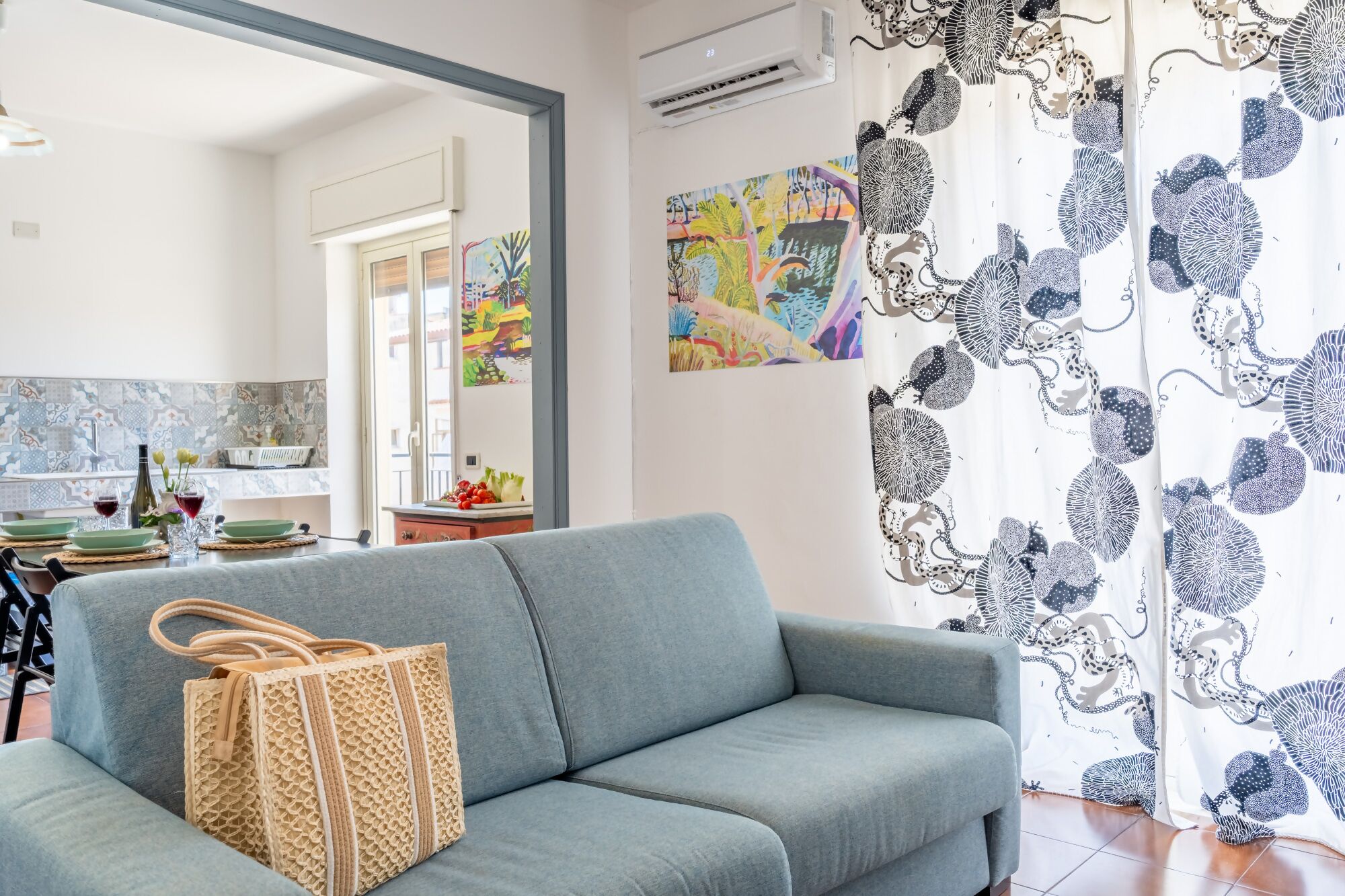 A living room with a grey sofa, a woven bag, and a colorful painting on the wall.