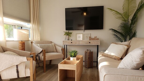 Ein modernes Wohnzimmer mit Sofa, Sesseln, Couchtisch, Wand-Fernseher und einer Zimmerpflanze.