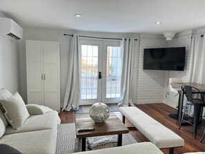 A modern living room with a sofa, a coffee table with a decorative item, a dining area with a table and chairs, and a TV mounted on the wall. - Lakefront Getaway Sparrow Lake Muskoka Beach House (Gravenhurst)