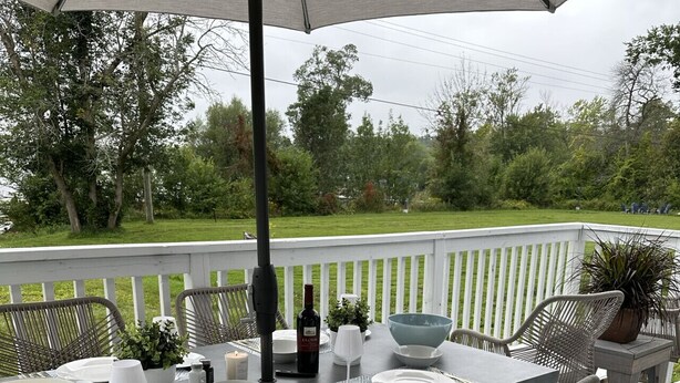 Une terrasse avec une table dressée pour le repas, entourée de chaises en osier, sous un grand parasol.