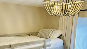 Une chambre avec un lit superposé, une petite table d’appoint en bois et un luminaire suspendu.