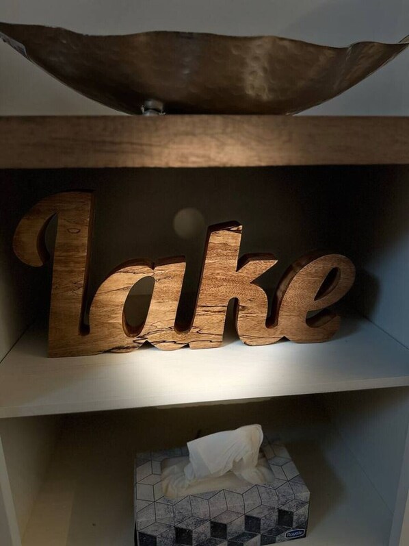Ein hölzernes Schild mit der leuchtenden Aufschrift 'Lake', platziert über einer gefliesten Schachtel mit Taschentüchern.