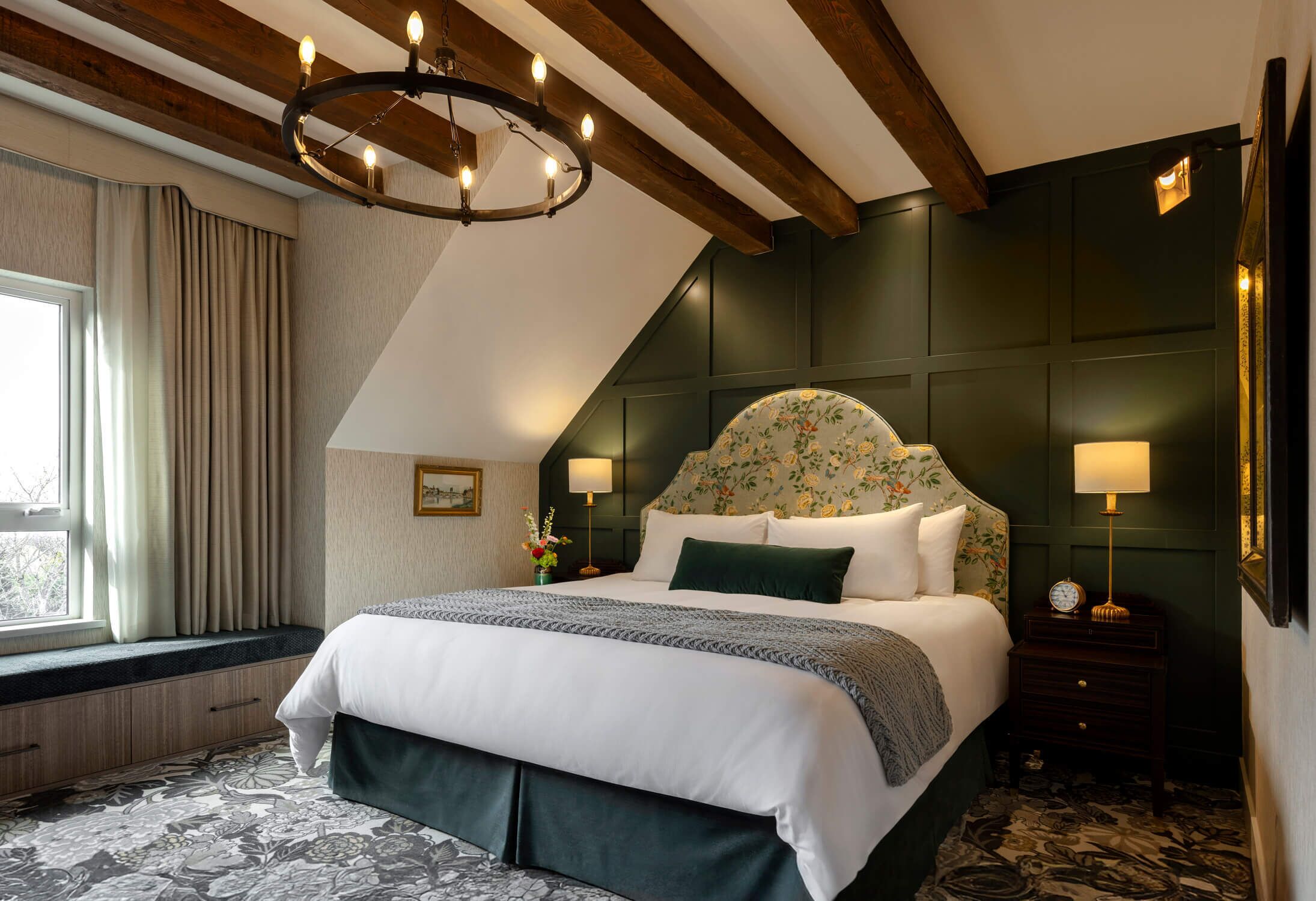 Una camera da letto con un letto grande, un lampadario, una finestra con tende e un comodino con una lampada.