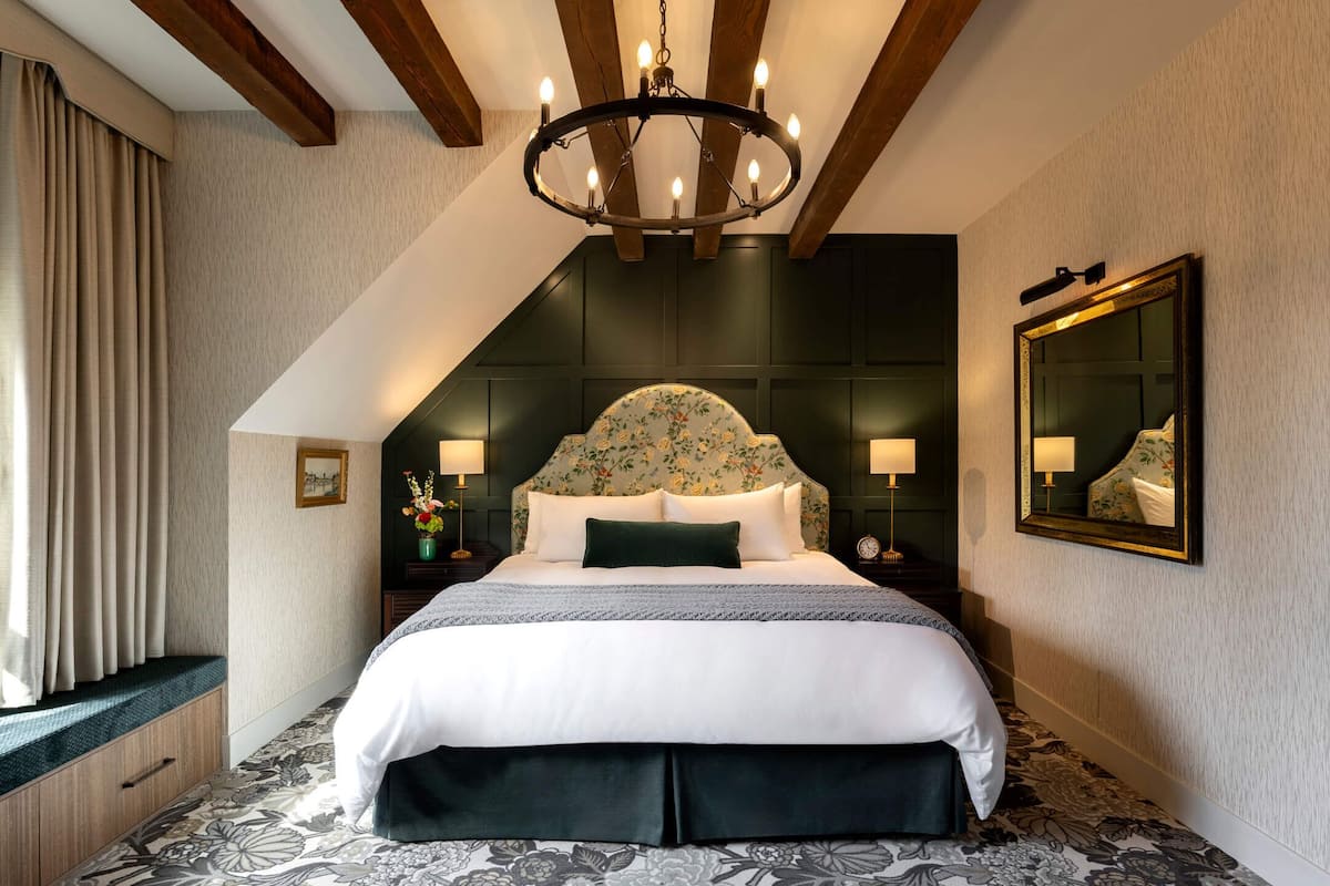 Une chambre à coucher avec un grand lit, un lustre, une tête de lit à motifs floraux et un miroir au mur.