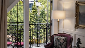 Ein Zimmer mit Blick auf Bäume und einem Balkon, ein violettes Sessel, eine Lampe und ein Büste auf einem Beistelltisch.