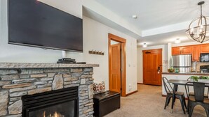 A modern living room with a stone fireplace, a flat-screen TV mounted above it, and a dining area with a table and chairs.