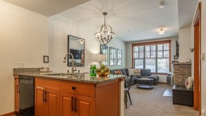 A spacious kitchen with granite countertops, a built-in dishwasher, and a large island. There is a dining area with a round table and chairs, and a living room with a sofa and a fireplace.
