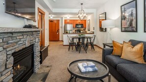 A living room with a fireplace, a dining area, and a kitchen in the background.