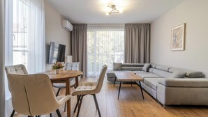 Una sala de estar moderna con una mesa de comedor de madera, dos sillas, un sofá gris y un televisor montado en la pared.