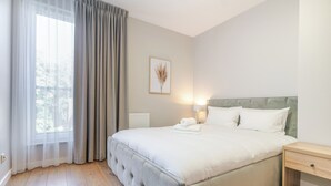 Un dormitorio ordenado con una cama grande, una mesita de noche y una ventana con cortinas.