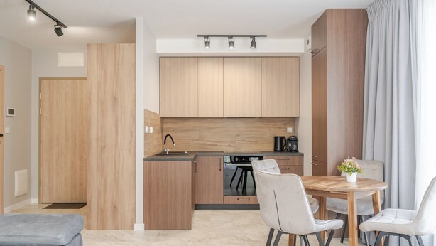 Una cocina moderna con armarios de madera, una isla central y un comedor con sillas blancas.