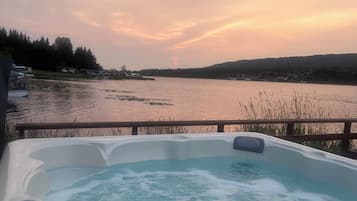 A hot tub with a view of a lake and hills during sunset.