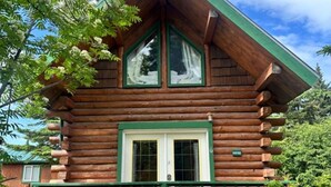 A log cabin with a green roof, a front porch, and a window with a white frame. - McNeil River Cabin, Homer Floatplane Lodge (Homer)
