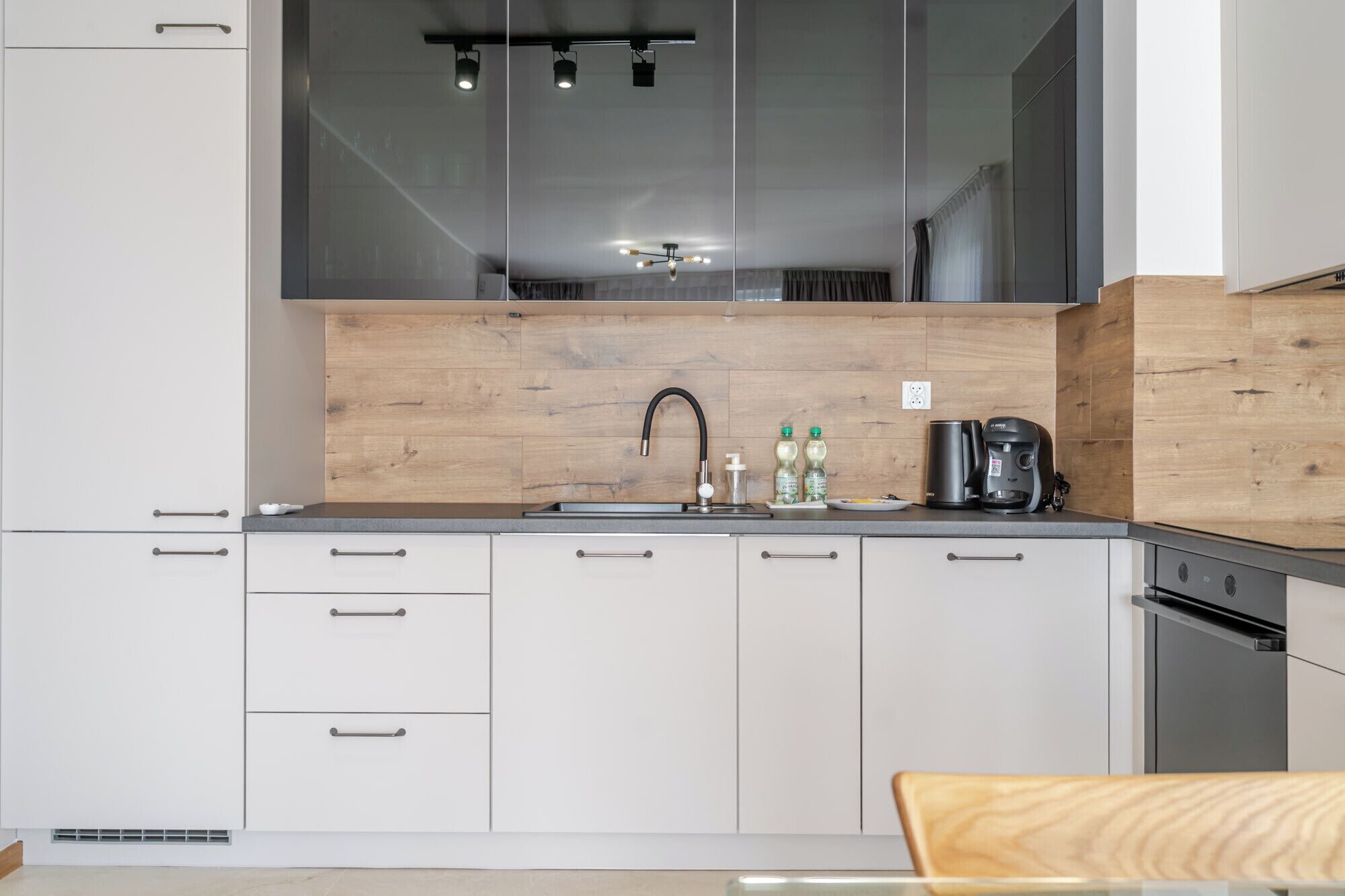 Een moderne keuken met witte kasten, een houten spatwand, een roestvrijstalen spoelbak en een koffiezetapparaat.
