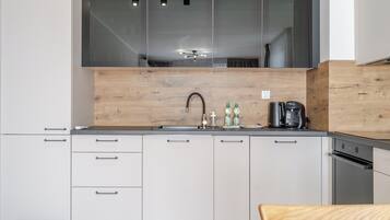 Een moderne keuken met witte kasten, een houten spatwand, een roestvrijstalen spoelbak en een koffiezetapparaat.