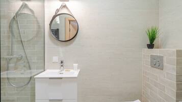 Une salle de bain moderne avec une douche à parois de verre, un meuble-lavabo blanc avec un miroir et une plante en pot accrochée au mur.