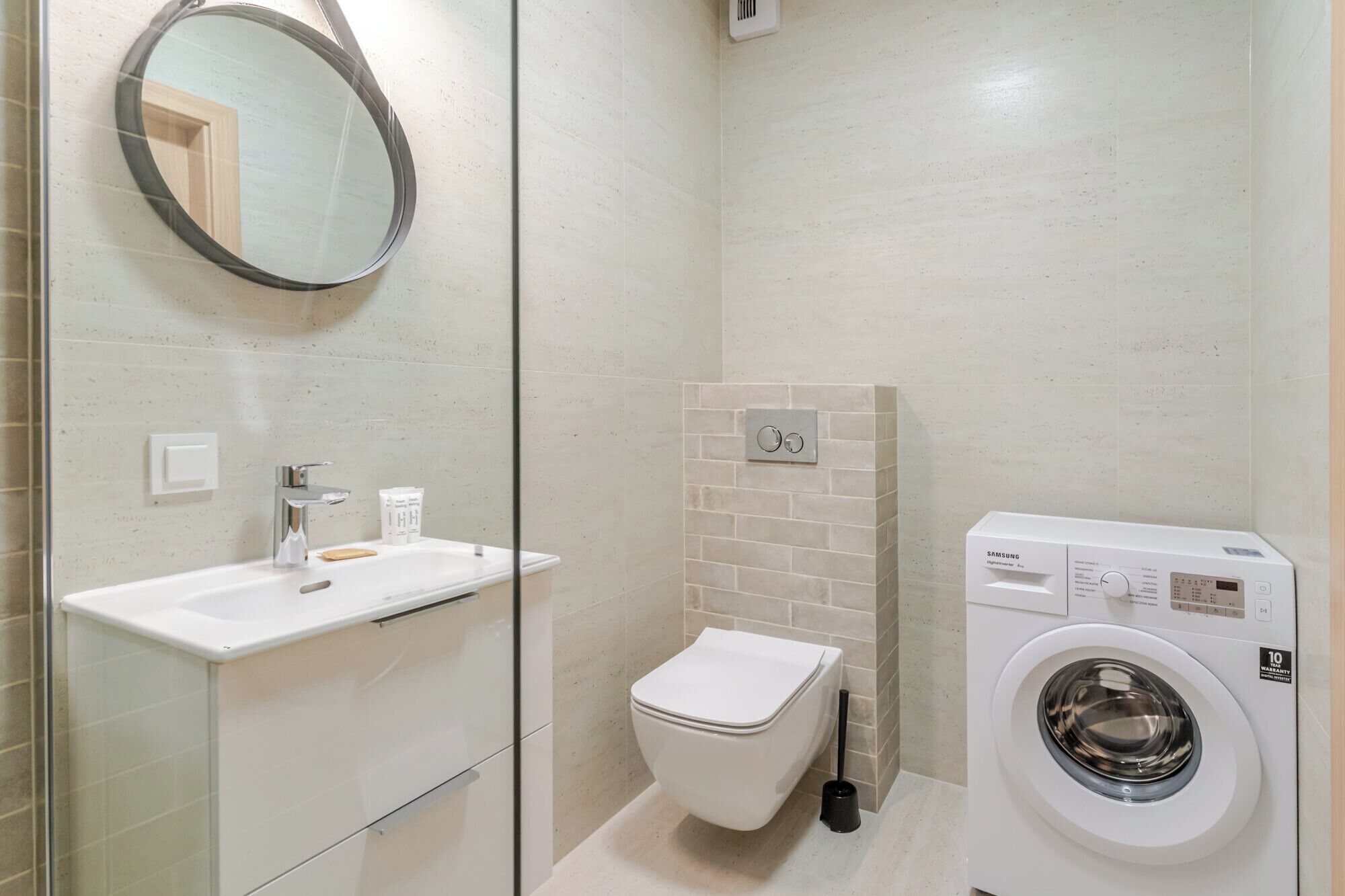 A modern bathroom with a glass shower enclosure, a toilet, a sink, and a washing machine.