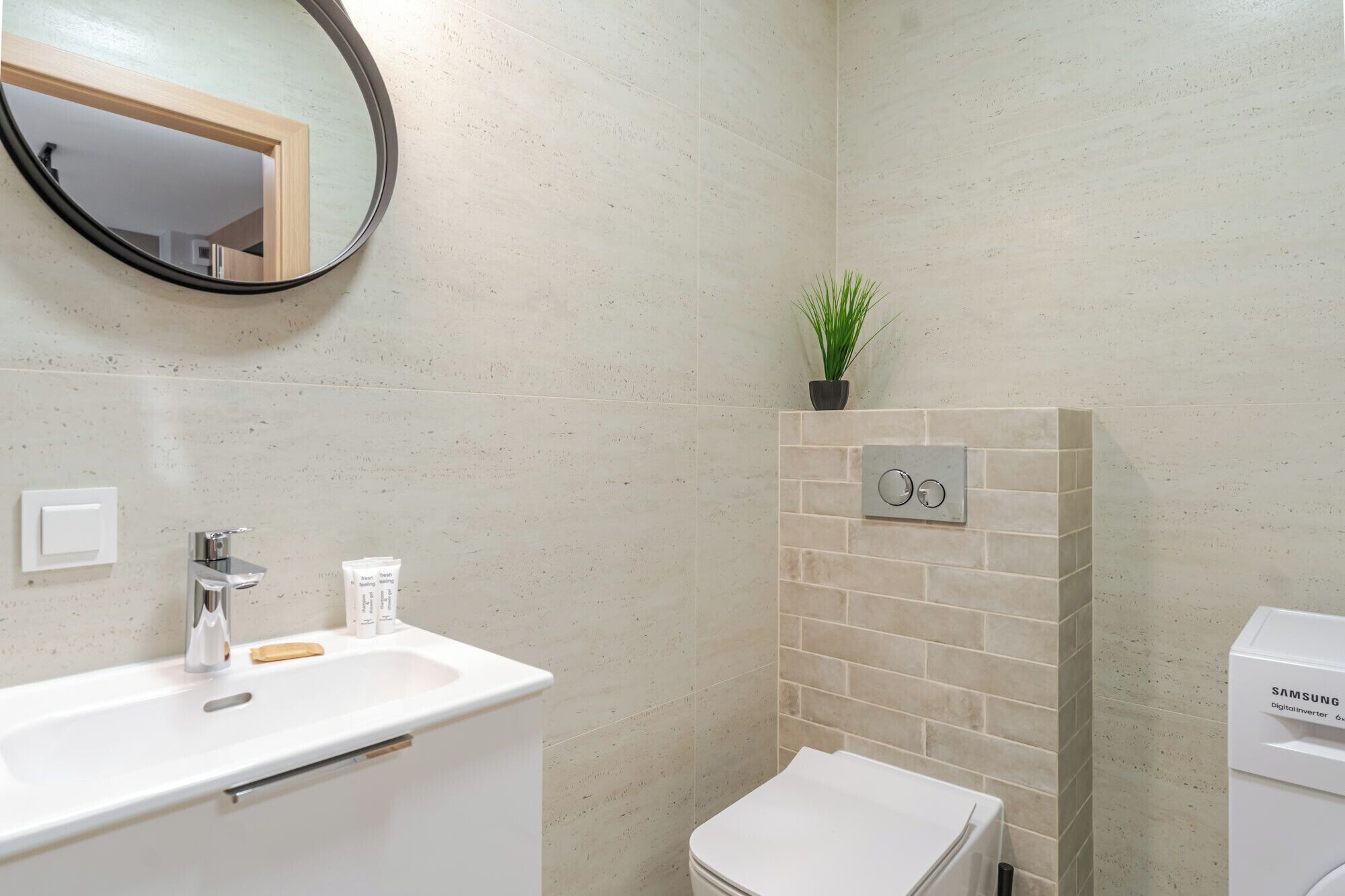 A bathroom with a sink, mirror, toilet, and a digital inverter on the wall.