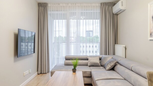 Un salon moderne avec un canapé beige, une table basse en bois et un téléviseur à écran plat fixé au mur.