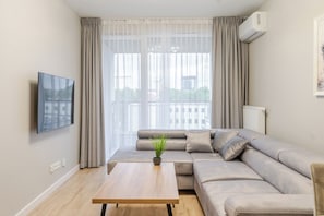 A modern living room with a beige sofa, a wooden coffee table, and a flat-screen TV mounted on the wall.