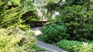 Een tuinpad dat leidt naar een houten constructie, omgeven door weelderige beplanting.