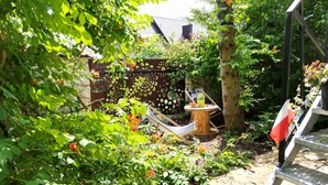 Een tuin met een houten schommel, een klein tafeltje met een gele pot, en een metalen ladder.
