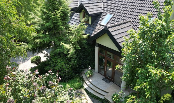 A house with a sloped roof, surrounded by lush greenery and trees.