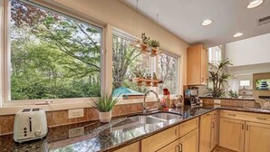 A modern kitchen with a large window, wooden cabinets, granite countertops, and various kitchen appliances.