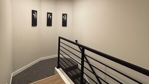 A staircase with a wooden floor and a black railing. There are three black wall art pieces on the wall. - Y Mountain Modern (Provo)